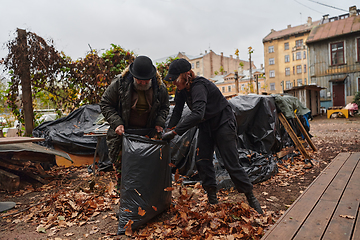 Image showing Father-daughter duo bonding in the garden as they work together to collect fallen leaves and fill up a bag on a crisp autumn day.