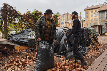 Image showing Father-daughter duo bonding in the garden as they work together to collect fallen leaves and fill up a bag on a crisp autumn day.