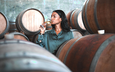 Image showing Woman doing wine tasting, drinking glass of chardonnay or sauvignon blanc in winery cellar amongst barrels on vineyard. Beautiful oenologist or sommelier enjoying a relaxing, luxury beverage indoors.