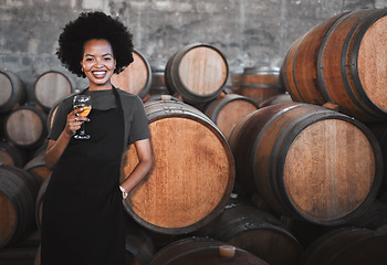 Image showing Portrait of a young woman winemaker standing with a glass with wooden barrel of red wine in a winery cellar or distillery. Entrepreneur or business owner working for startup success business success