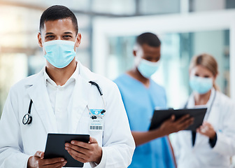 Image showing A successful male doctor browsing the internet, using a tablet and wearing a mask inside a hospital. Portrait of a healthcare professional searching covid, flu or disease on a digital device