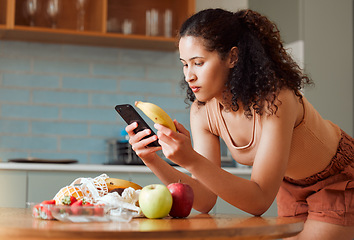 Image showing Woman reading phone, researching a diet with fresh fruit while relaxing in a kitchen at home. Young female searching for a recipe, cleanse or detox online. Lady checking nutritional value of a banana