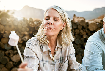 Image showing Senior woman eating marshmallow with regret, relaxing by the campfire after her mountain adventure in the outdoors nature. Female enjoying wellness lifestyle, resting after hiking trip with friends