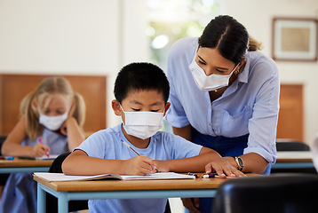 Image showing Covid, education and learning with a teacher wearing a mask and helping a male student in class during school. Young boy studying in a classroom with help from an educator while sitting at his desk.