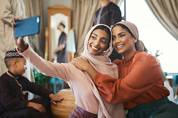 Image showing Muslim sisters taking selfies in traditional Islamic head scarf inside a happy family home together. Beautiful young women who are proud of their religion post photos of Eid Ramadan on social media