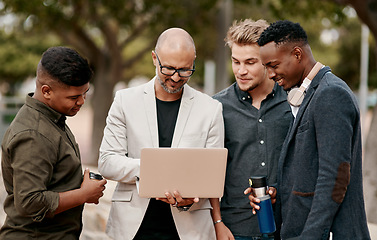 Image showing A team leader coaching his staff outdoors, standing and using a laptop. A group of male designers working on a start up project, looking at content on a computer outside, teamwork in the open air.