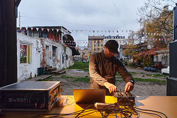 Image showing A young man is entertaining a group of friends in the backyard of his house, becoming their DJ and playing music in a casual outdoor gathering