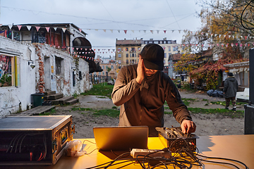 Image showing A young man is entertaining a group of friends in the backyard of his house, becoming their DJ and playing music in a casual outdoor gathering