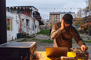 Image showing A young man is entertaining a group of friends in the backyard of his house, becoming their DJ and playing music in a casual outdoor gathering