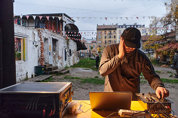 Image showing A young man is entertaining a group of friends in the backyard of his house, becoming their DJ and playing music in a casual outdoor gathering