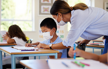 Image showing Education, covid and learning with face mask on boy doing school work in classroom, teacher helping student while writing in class. Elementary child wearing protection to stop the spread of a virus