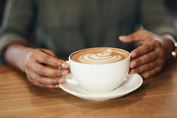 Image showing Woman drinking coffee, sitting and relaxing in a cafe. Close up of an African lady with cappuccino, holding a cup at a restaurant table. Enjoying a hot beverage while on a break, taking time for rest