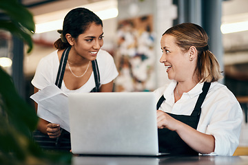 Image showing Small business owner working on a budget strategy or ordering stock online with an employee using a laptop in her store. Female entrepreneur talking to a worker about startup growth and sales
