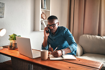 Image showing Young entrepreneur on his phone while taking notes at his desk. Professional man working remote from home with technology. African American male has a business meeting on an audio call.