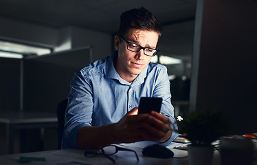 Image showing Confused businessman texting on his phone at the office at night. Handsome, confident and corporate caucasian male looking at messages from coworkers while working overtime and feeling unsure