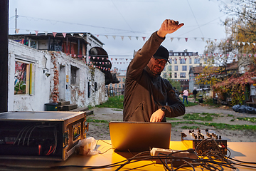 Image showing A young man is entertaining a group of friends in the backyard of his house, becoming their DJ and playing music in a casual outdoor gathering