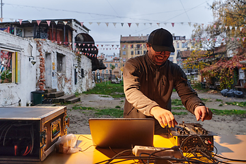 Image showing A young man is entertaining a group of friends in the backyard of his house, becoming their DJ and playing music in a casual outdoor gathering