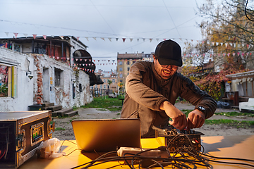 Image showing A young man is entertaining a group of friends in the backyard of his house, becoming their DJ and playing music in a casual outdoor gathering