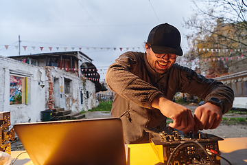 Image showing A young man is entertaining a group of friends in the backyard of his house, becoming their DJ and playing music in a casual outdoor gathering