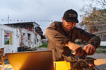 Image showing A young man is entertaining a group of friends in the backyard of his house, becoming their DJ and playing music in a casual outdoor gathering