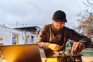 Image showing A young man is entertaining a group of friends in the backyard of his house, becoming their DJ and playing music in a casual outdoor gathering