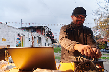 Image showing A young man is entertaining a group of friends in the backyard of his house, becoming their DJ and playing music in a casual outdoor gathering