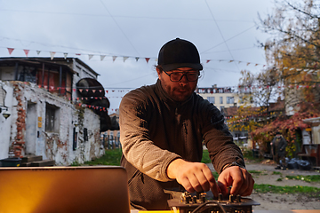 Image showing A young man is entertaining a group of friends in the backyard of his house, becoming their DJ and playing music in a casual outdoor gathering