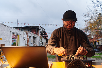 Image showing A young man is entertaining a group of friends in the backyard of his house, becoming their DJ and playing music in a casual outdoor gathering