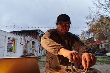 Image showing A young man is entertaining a group of friends in the backyard of his house, becoming their DJ and playing music in a casual outdoor gathering