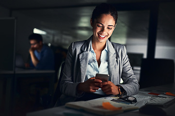 Image showing Woman reading text late on phone, smiling at a message and looking at social media posts online while working in a dark office at night. Happy corporate worker checking emails and doing overtime