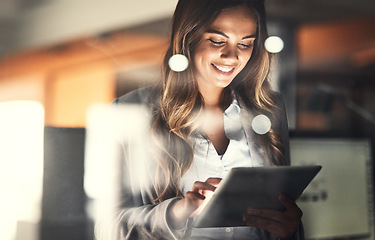 Image showing Working late, overtime and dedication with a happy, positive and motivated business woman working on a tablet in her office. Young female executive smiling while feeling dedicated and determined