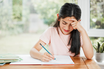 Image showing Stressed, frustrated and unhappy girl writing homework with a difficult task alone at home. Tired school child studying for a hard exam. Upset student learning with homeschooling education.