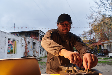 Image showing A young man is entertaining a group of friends in the backyard of his house, becoming their DJ and playing music in a casual outdoor gathering