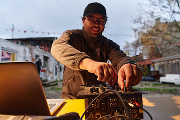 Image showing A young man is entertaining a group of friends in the backyard of his house, becoming their DJ and playing music in a casual outdoor gathering