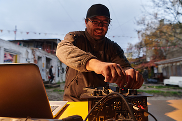 Image showing A young man is entertaining a group of friends in the backyard of his house, becoming their DJ and playing music in a casual outdoor gathering