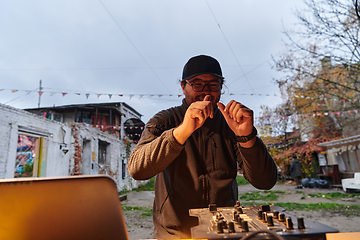 Image showing A young man is entertaining a group of friends in the backyard of his house, becoming their DJ and playing music in a casual outdoor gathering