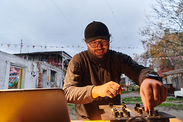 Image showing A young man is entertaining a group of friends in the backyard of his house, becoming their DJ and playing music in a casual outdoor gathering