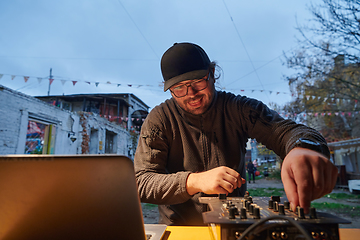 Image showing A young man is entertaining a group of friends in the backyard of his house, becoming their DJ and playing music in a casual outdoor gathering