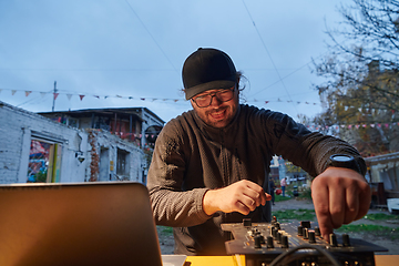 Image showing A young man is entertaining a group of friends in the backyard of his house, becoming their DJ and playing music in a casual outdoor gathering