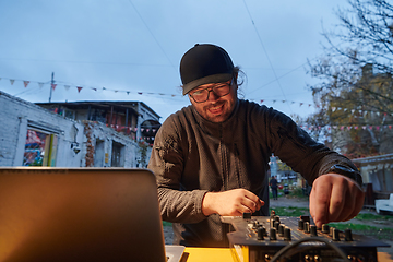 Image showing A young man is entertaining a group of friends in the backyard of his house, becoming their DJ and playing music in a casual outdoor gathering