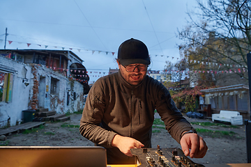 Image showing A young man is entertaining a group of friends in the backyard of his house, becoming their DJ and playing music in a casual outdoor gathering