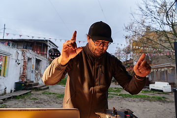 Image showing A young man is entertaining a group of friends in the backyard of his house, becoming their DJ and playing music in a casual outdoor gathering