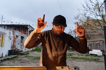 Image showing A young man is entertaining a group of friends in the backyard of his house, becoming their DJ and playing music in a casual outdoor gathering