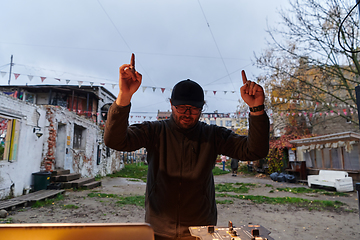 Image showing A young man is entertaining a group of friends in the backyard of his house, becoming their DJ and playing music in a casual outdoor gathering