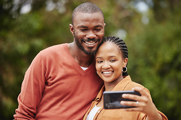 Image showing Trendy, modern couple taking selfie on phone while on a romantic date in a park and sharing relationship status on social media app. Smiling, in love married husband and wife capturing happy memories