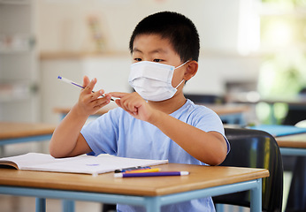 Image showing Education, covid and learning with face mask on boy doing school work in classroom, writing and counting at his desk in elementary class. Asian child wearing protection to stop the spread of virus