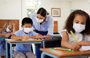 Image showing Covid, education and learning with a teacher wearing a mask and helping a male student in class during school. Young boy studying in a classroom with help from an educator while sitting at his desk