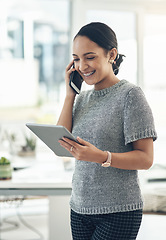 Image showing Professional smiling businesswoman talking on phone call with client in modern office. Young design employee working on appointment booking on tablet standing in casual startup company