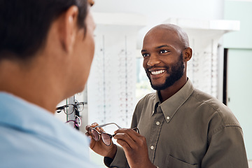 Image showing Shopping for glasses at an optician retail store with a smiling man trying to search for a pair. Optometrist and customer service employee selling a happy buying client new and modern spectacles