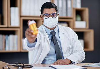 Image showing Doctor selling medicine for covid at medical consultation, sitting behind office desk in hospital. Healthcare professional consulting offer bottle of pills for treatment, wearing mask for protection.